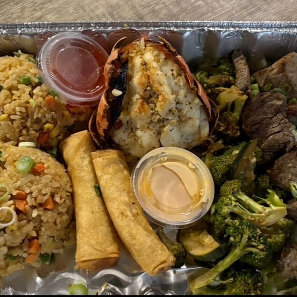 A takeout container with fried rice, lobster tail, egg rolls, beef, and broccoli.